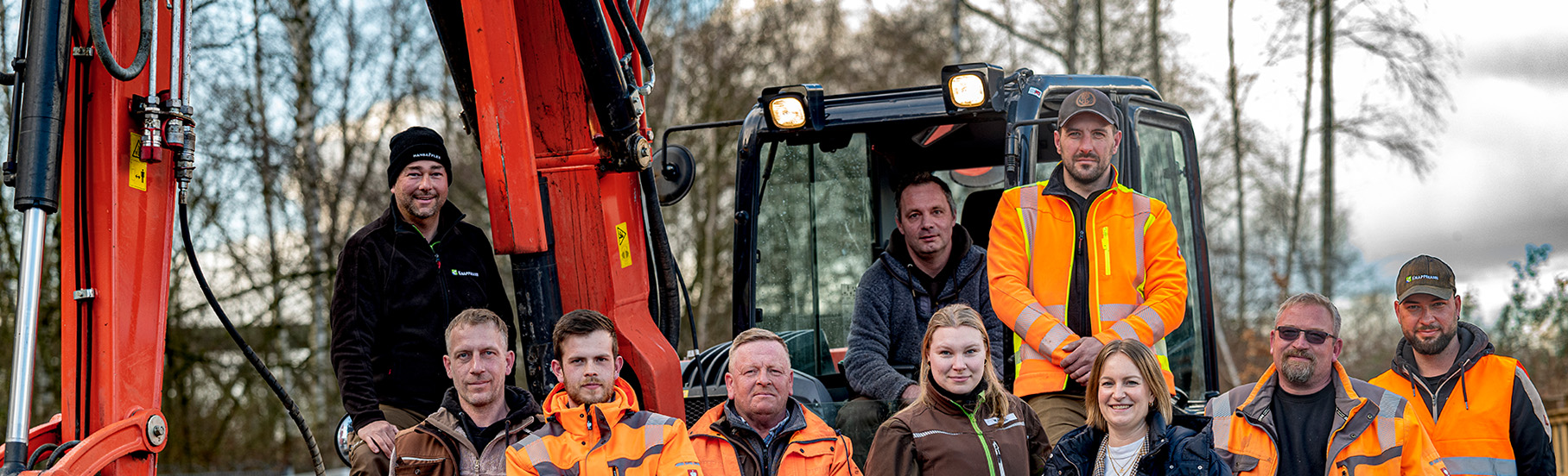 Team des GaLaBau Betriebs stehen vor einem Bagger