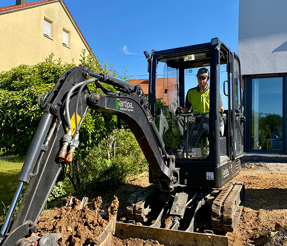 Landschaftsgärtner im Bagger verrichtet Arbeit im Privatgarten